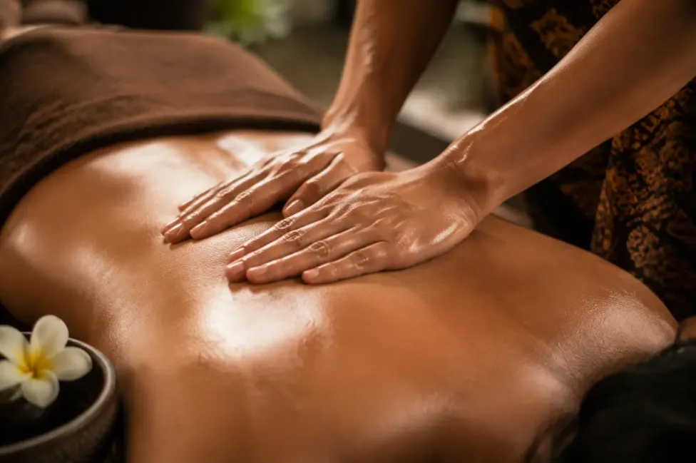 Close-up of shoulders and back being gently massaged with oil under soft indoor lighting in villa sanur, bali