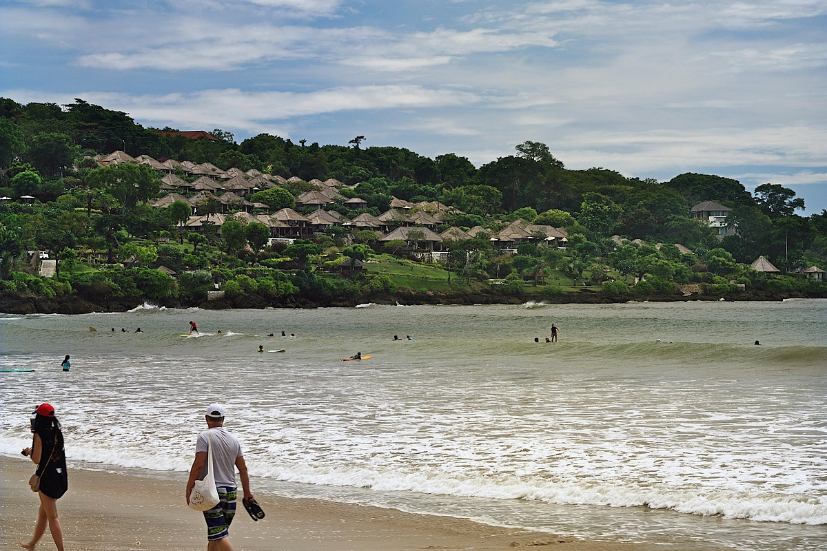 A tourist takes a leisurely stroll along the beach, enjoying views of cliffs and pristine white sand at Kedonganan Beach, Jimbaran, Bali.